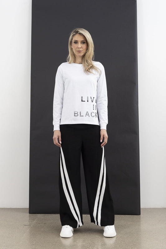 Woman wearing a light gray sweatshirt with text and black pants with white stripes, standing against a black and white background.