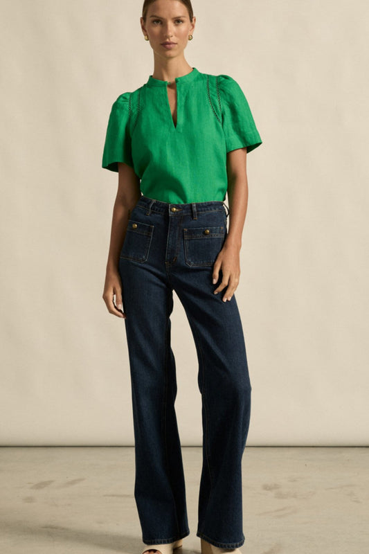 Woman wearing a green blouse and dark blue jeans against a neutral background