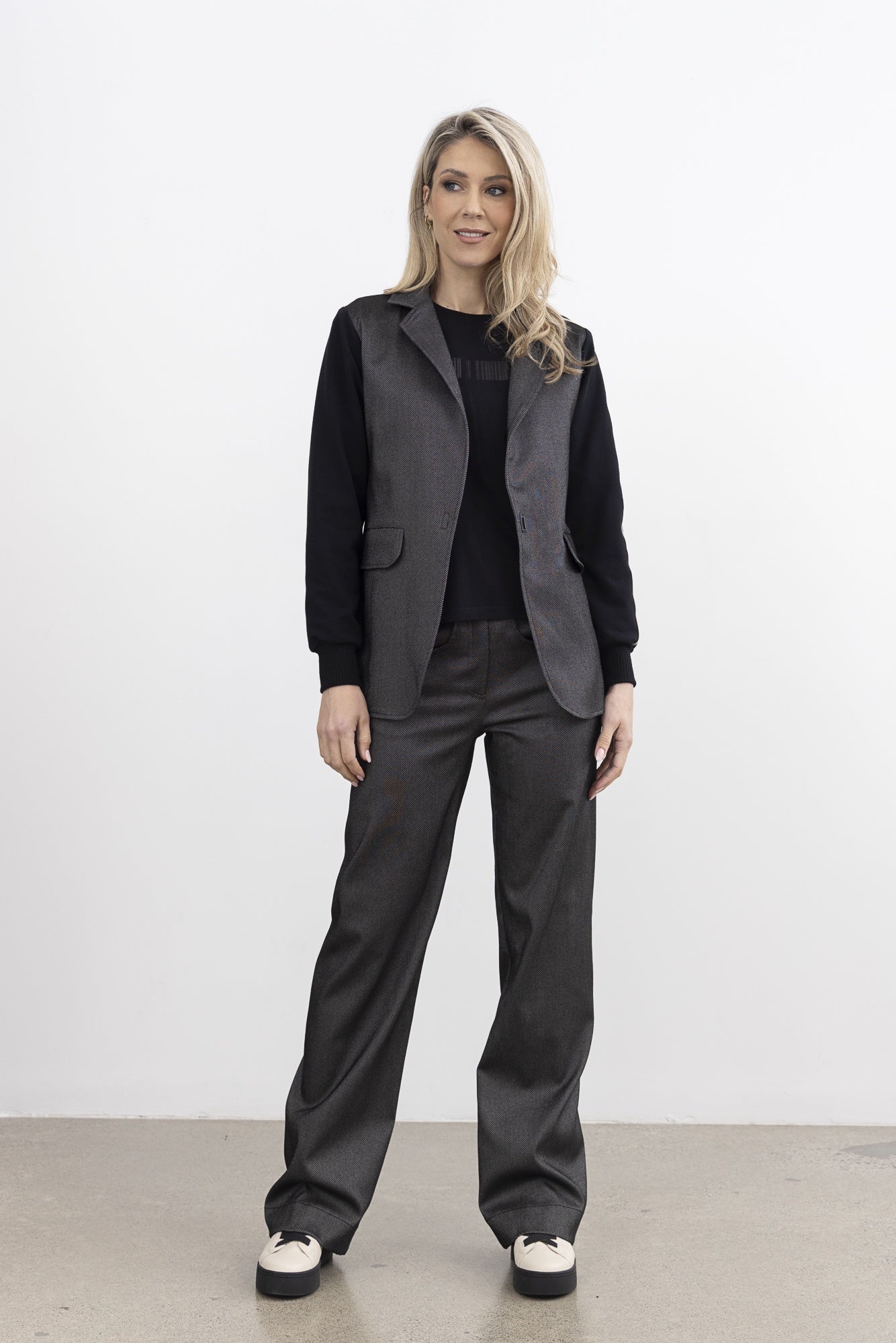 Woman wearing a dark gray outfit with a jacket and pants against a white background