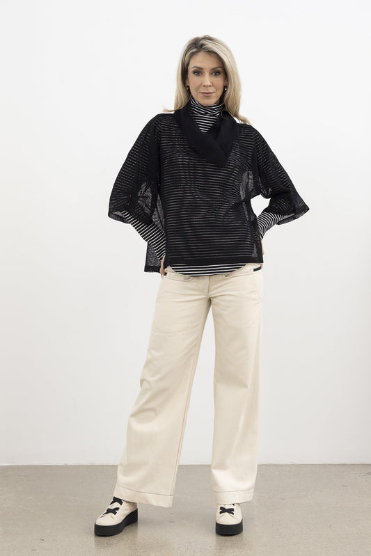 Woman wearing a black striped sweater and beige pants against a white background