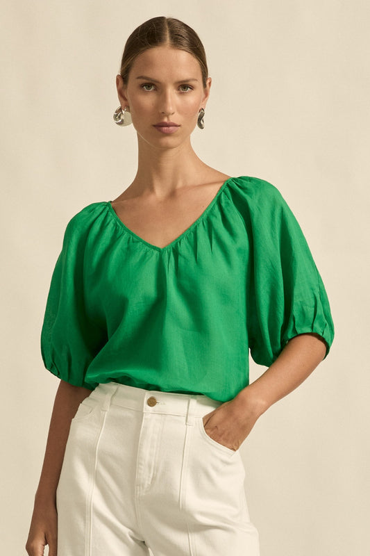 Woman wearing a green blouse and white pants against a beige background